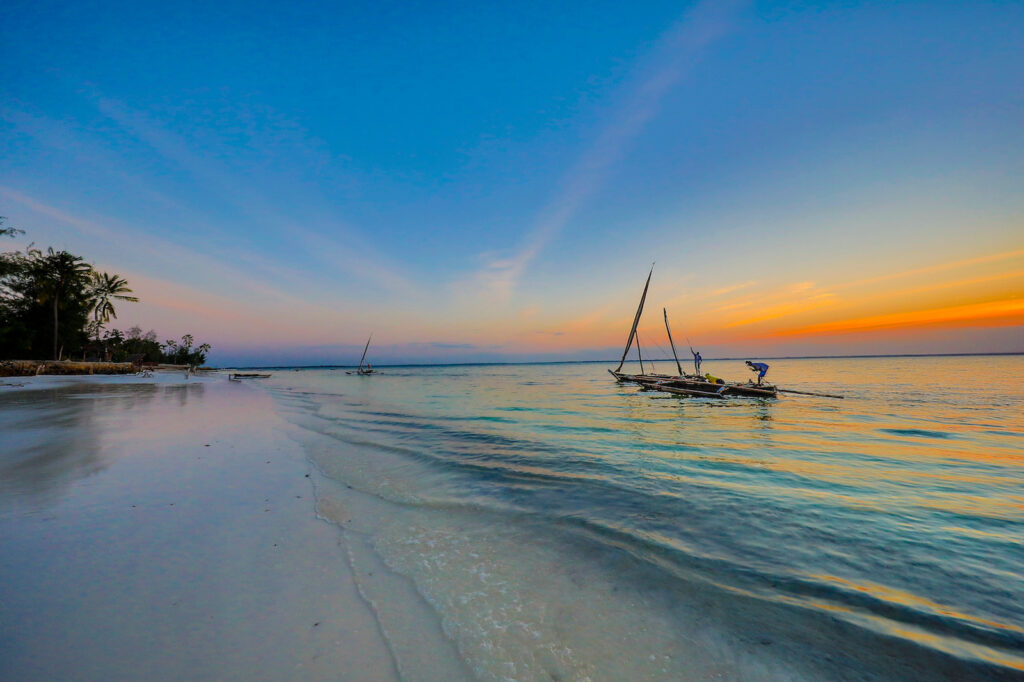 A wooden boat floating in Zanzibar’s turquoise waters with a golden sunset sky in the background.