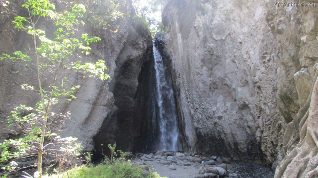 A scenic waterfall inside Arusha National Park, Tanzania, surrounded by green vegetation.