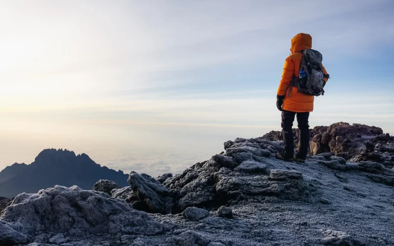 Climber standing at the summit of Kilimanjaro, looking down at the clouds after a successful trek