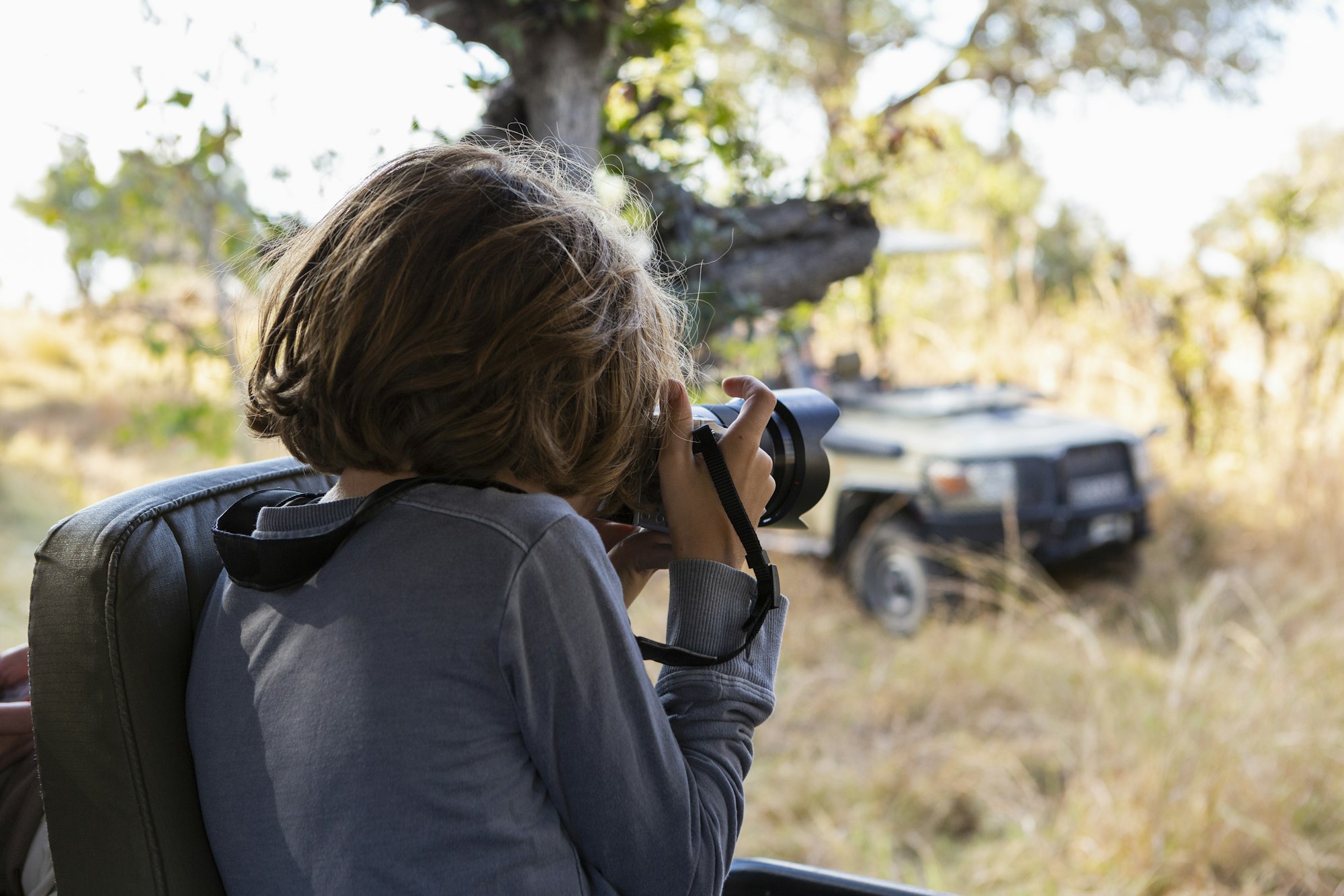 young boy using a large camera during a jeep drive on safari