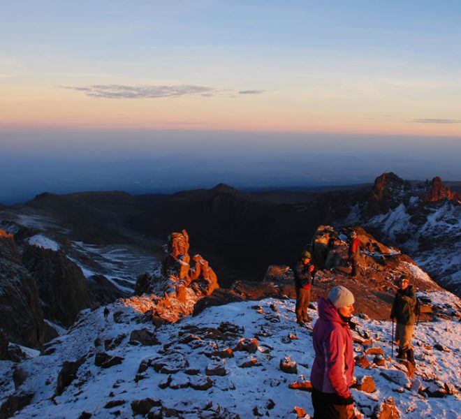 Three climbers standing on Mount Kilimanjaro summit at sunrise, bathed in golden light