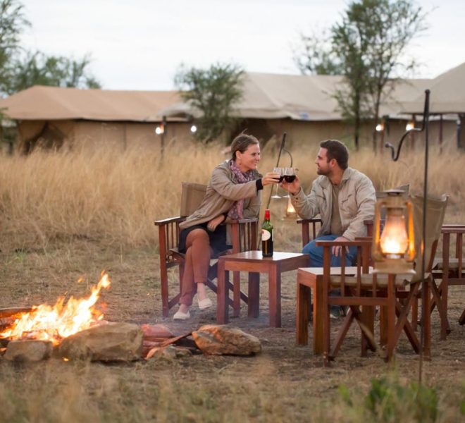 a couple in the evening fire enjoying a drink on their honeymoon safari