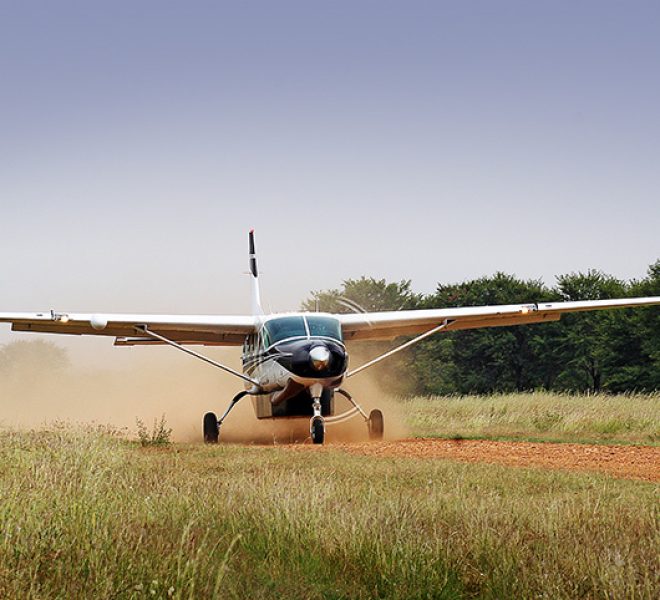 Small plane landing on a dirt airstrip in Serengeti National Park, surrounded by open savannah.