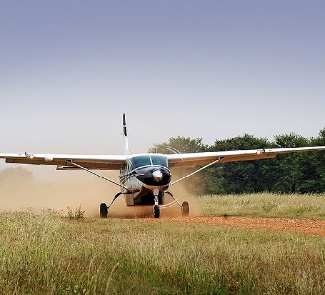 Small plane landing on a dirt airstrip in Serengeti National Park, surrounded by open savannah.