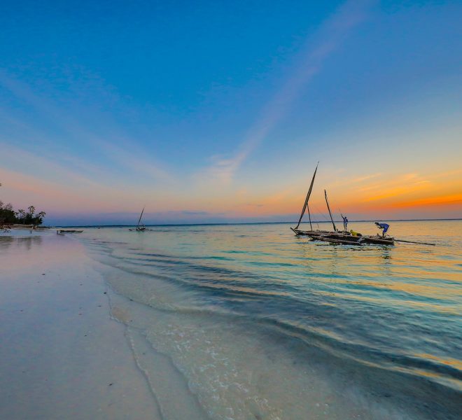 A wooden boat floating in Zanzibar’s turquoise waters with a golden sunset sky in the background.