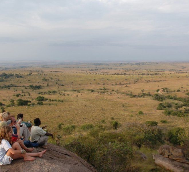 a group of tourists on a rock viewing the great serengeti plains